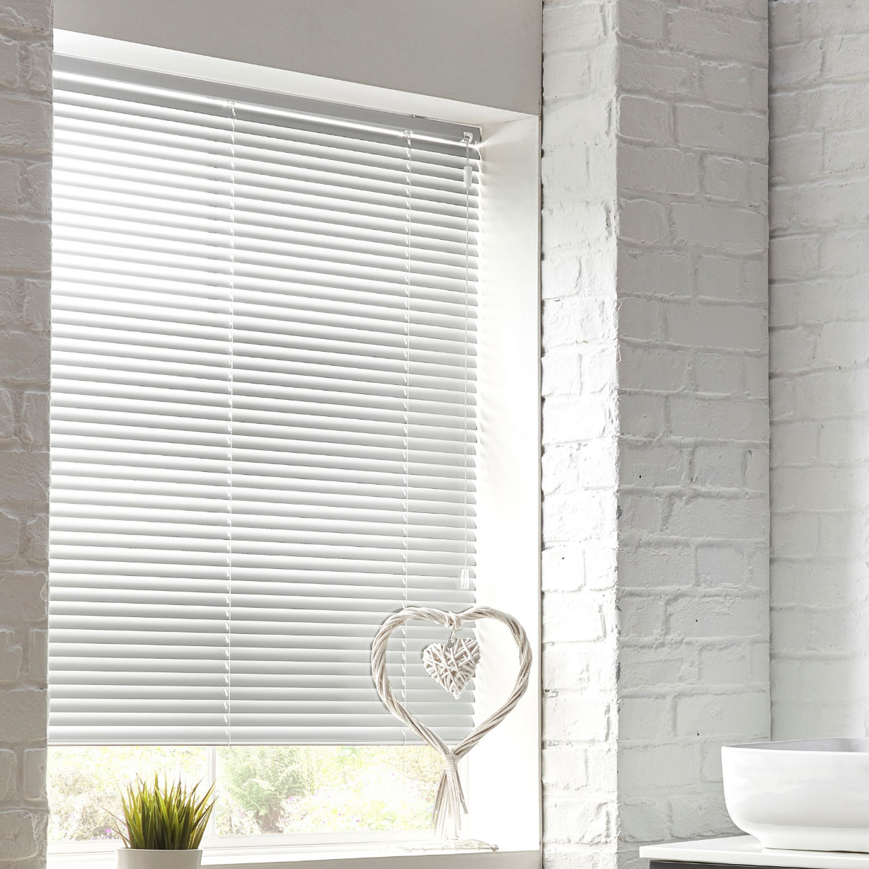 White aluminium venetian blind in white painted brick room with love heart ornament decoration on window sill