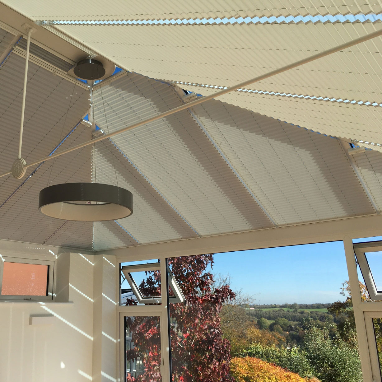 Grey white neutral conservatory blinds on the roof windows of a conservatory with a countryside view from the front