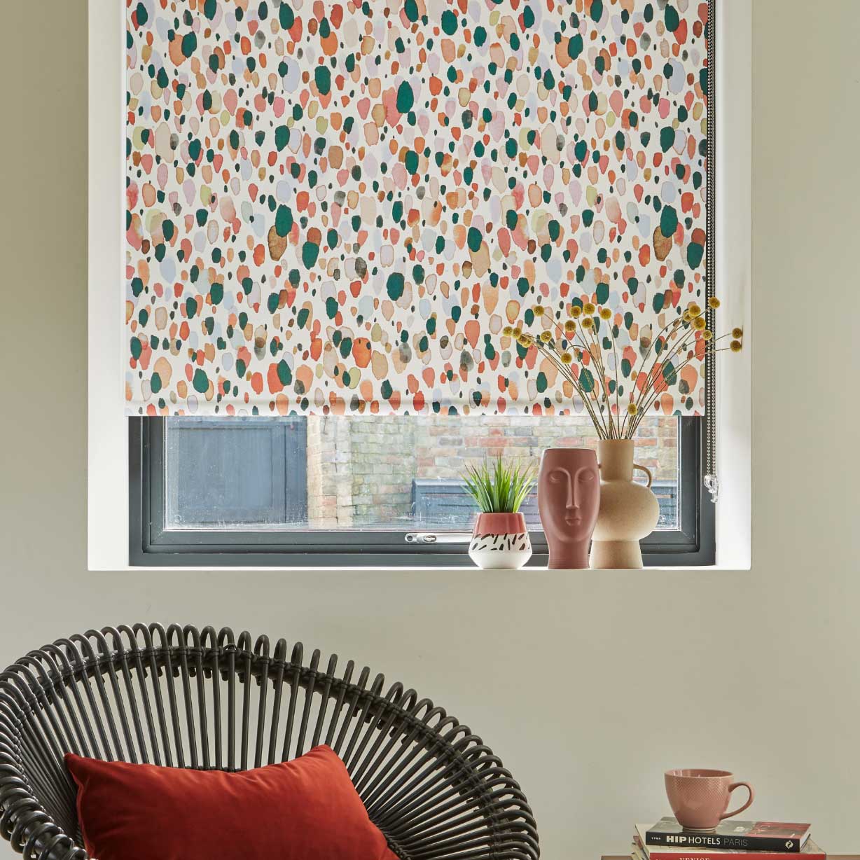 Multi-coloured roller blind in neutral room with contemporary chair and orange-red cushion