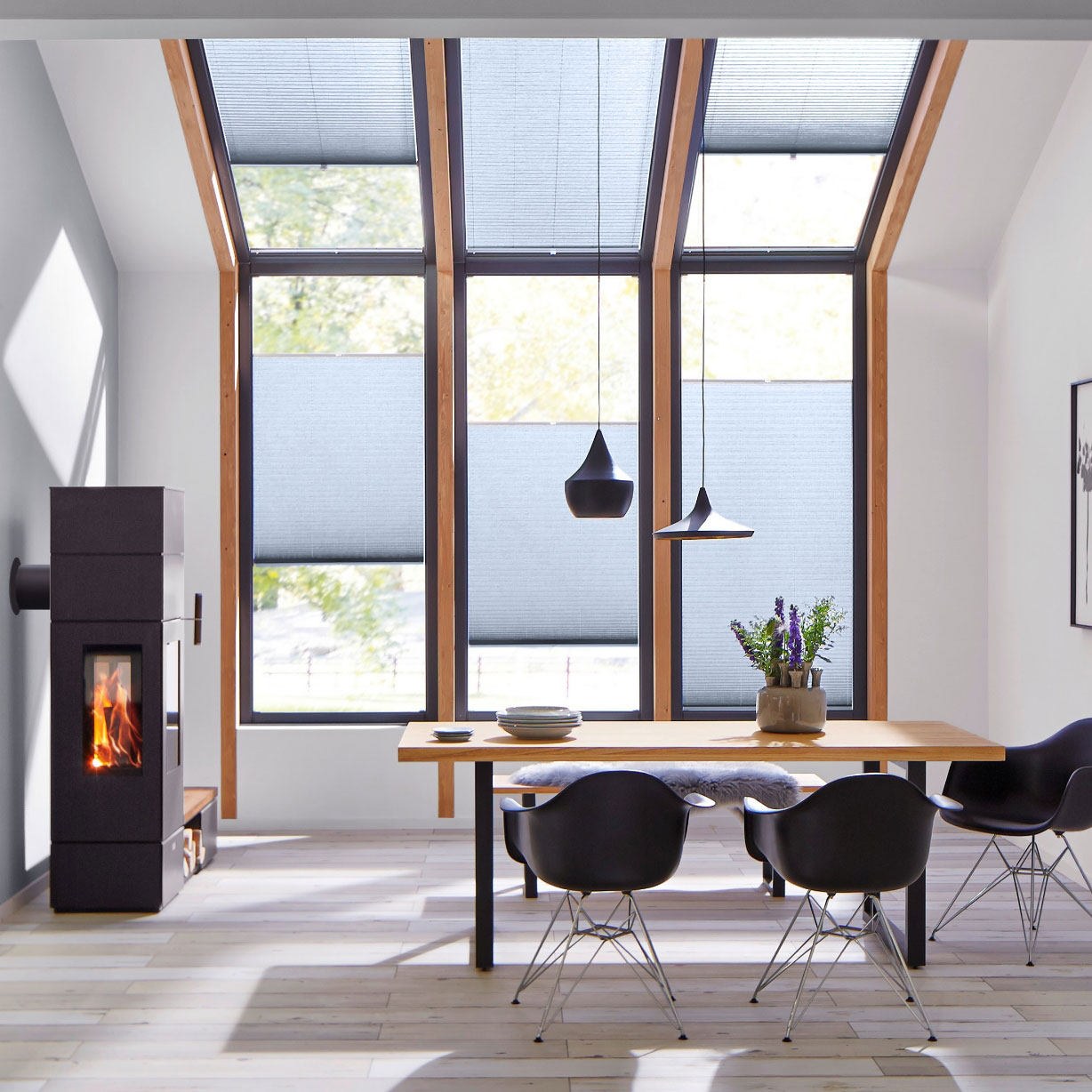Grey pleated blinds on wall and sloping ceiling windows with a woodburner and dining table